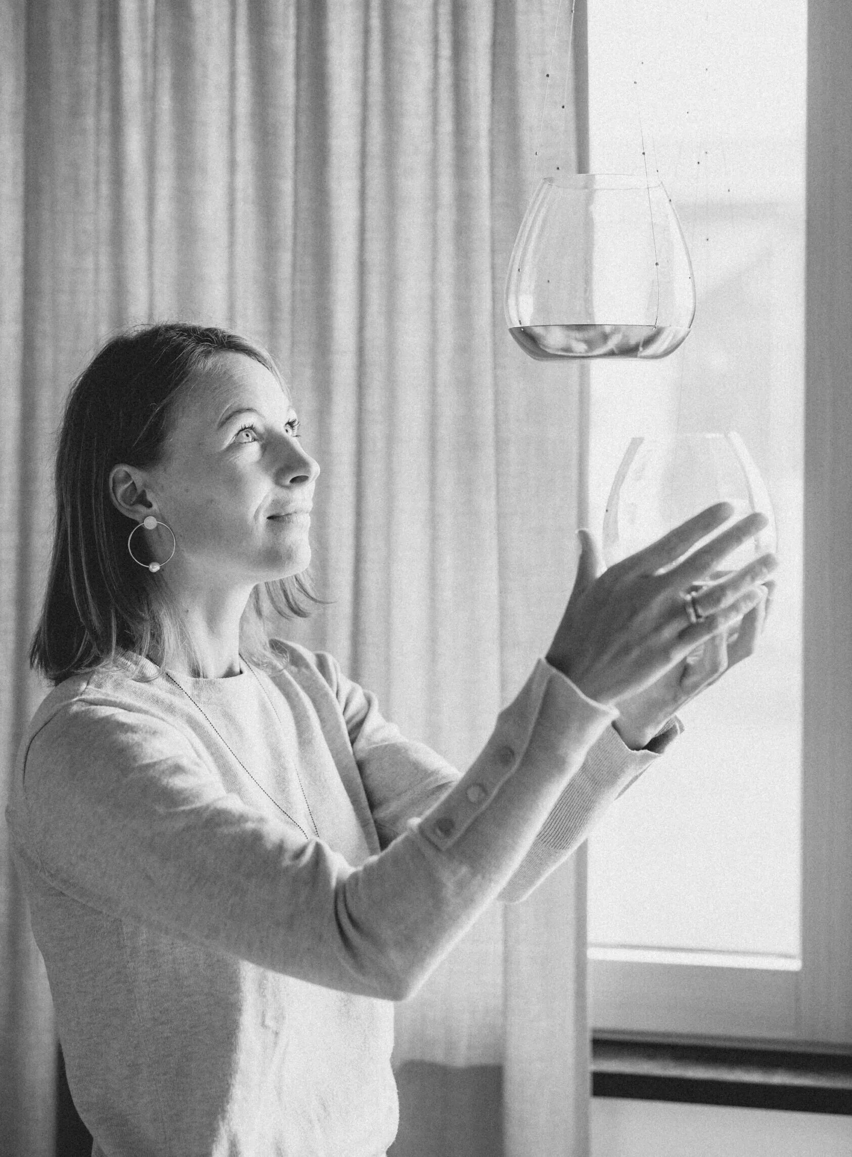 Frau greift nach hängenden Glasvasen am Fenster, Schwarz-Weiß