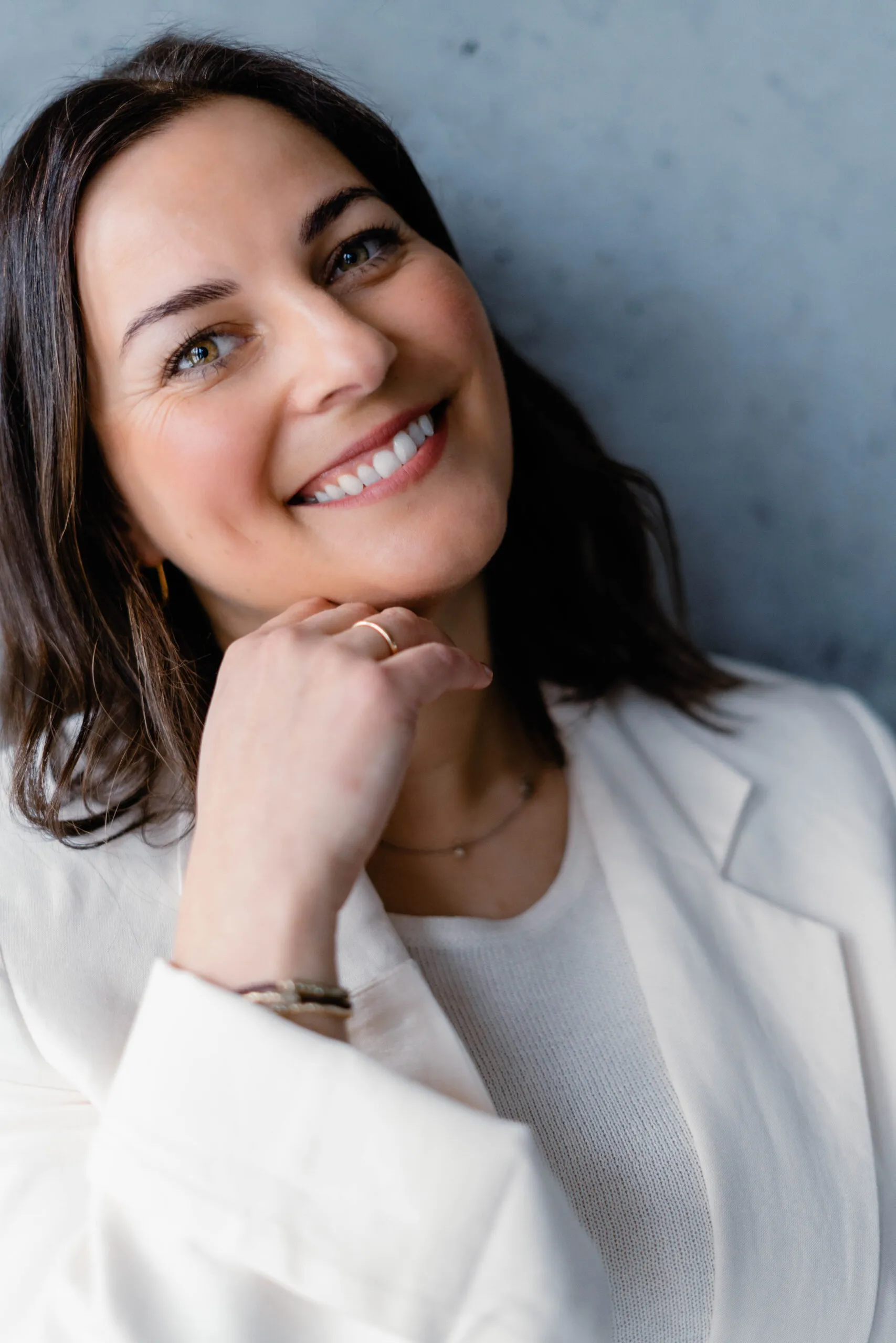 Julia Bechter, lächelnd im weißen Blazer vor einer Betonwand