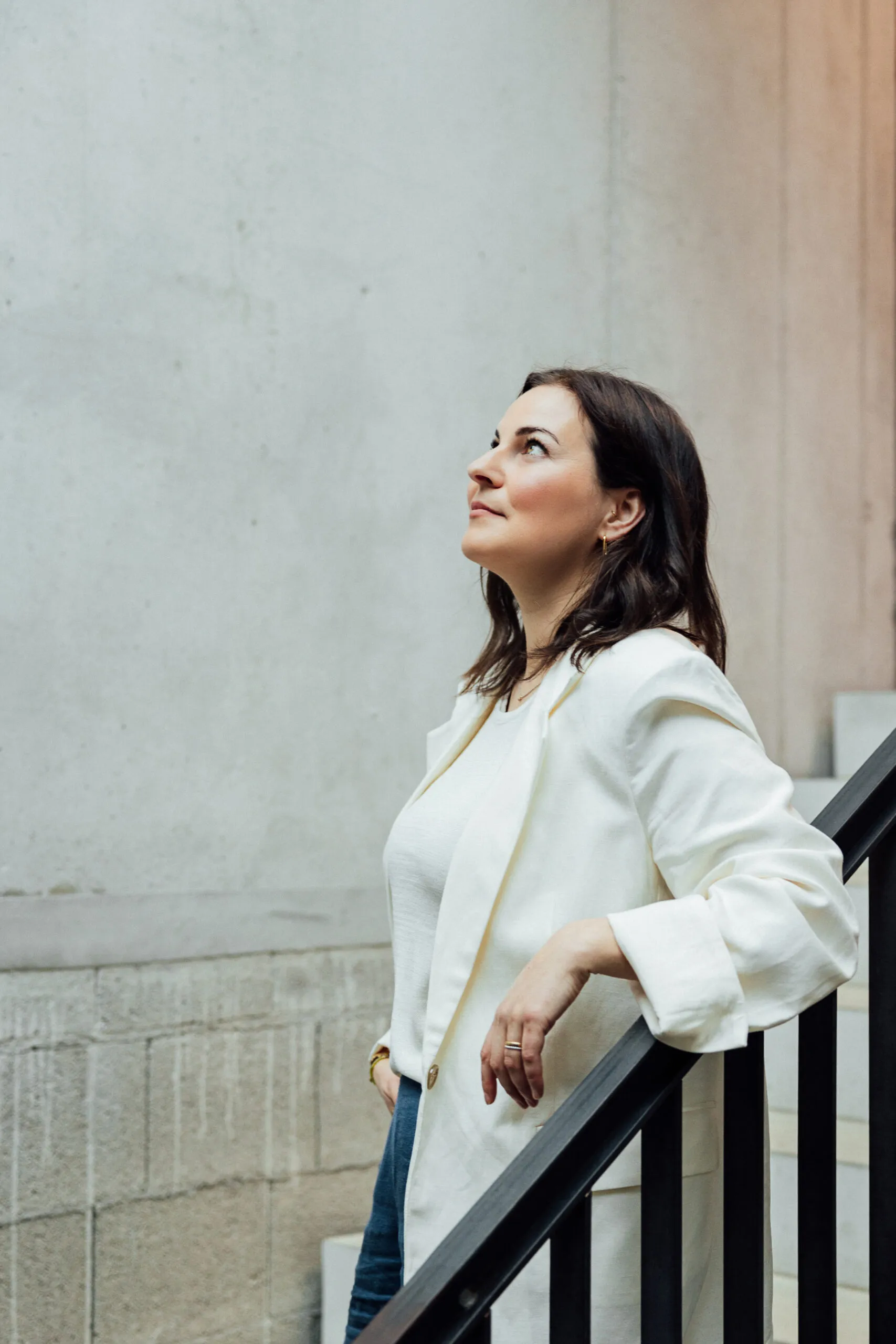 Julia Bechter in weißer Bluse, an ein Treppengeländer gelehnt, Blick nach oben