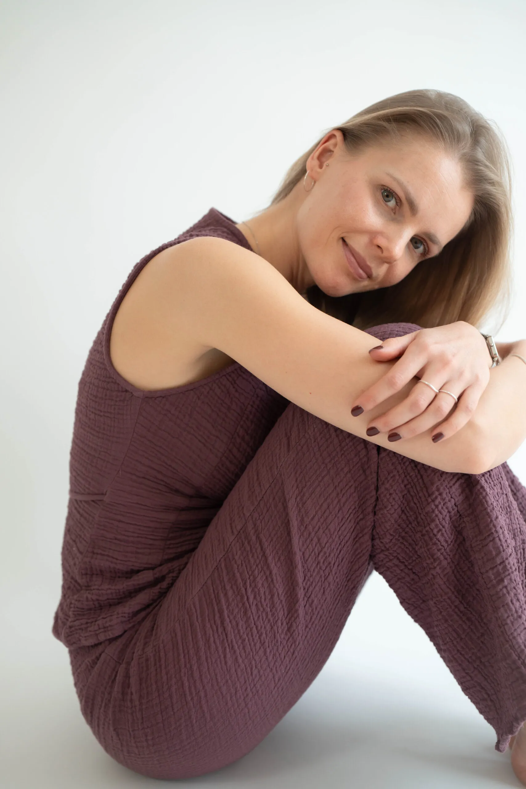 Frau in weinrotem Jumpsuit sitzt ruhig am Boden